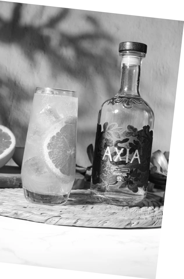 Black and white picture of a bottle of Axia Spirit next to an Aegean Paloma cocktail on a table