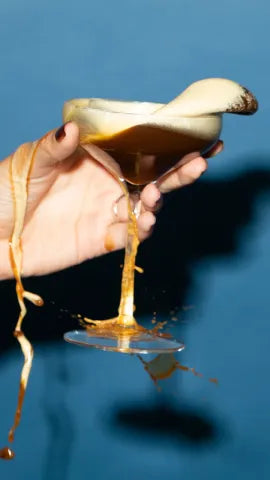 Hand holding Axia Spirit Axpresso Martini Cocktail, spilling out of glass, on blue background
