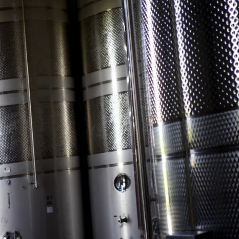 A detailed view of several large, cylindrical stainless steel tanks with textured, dimpled surfaces reflecting light for the mastiha spirit resting process