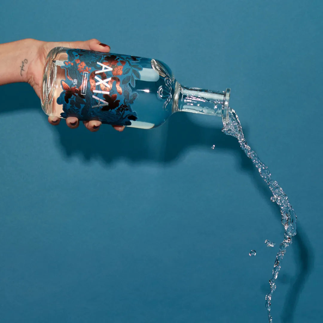 Hand holding a bottle of Axia Mastiha Spirit being poured on a blue background