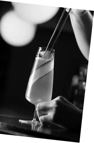 Black and white picture of an Axia Greek Mastiha Spirit and Oriole Bar Champagne Cocktail with cucumber on a wooden counter